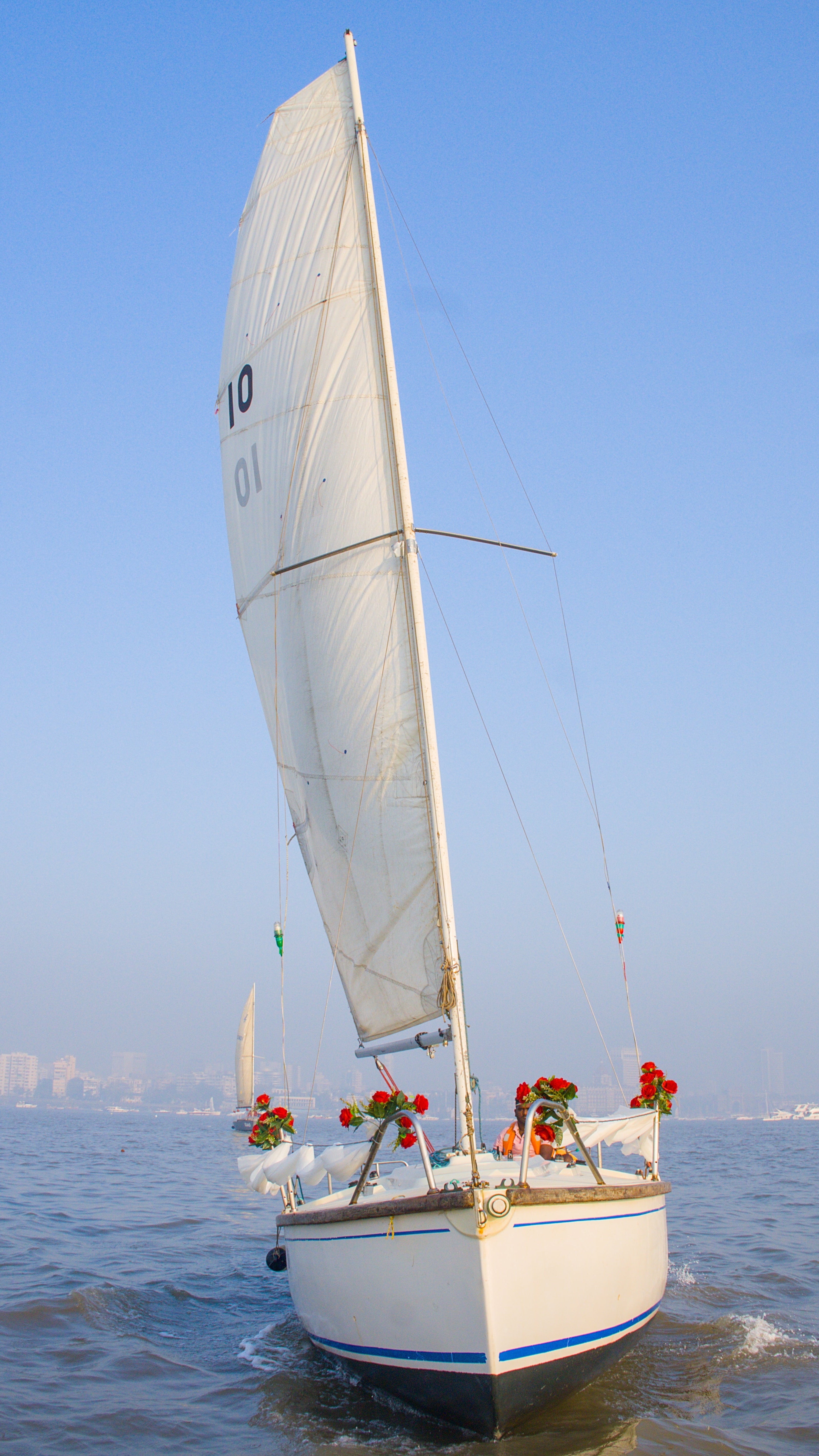 Sailboat with a white sail on a body of water under a clear blue sky.